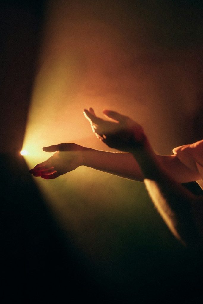 Two hands reaching into a bright beam of warm golden light